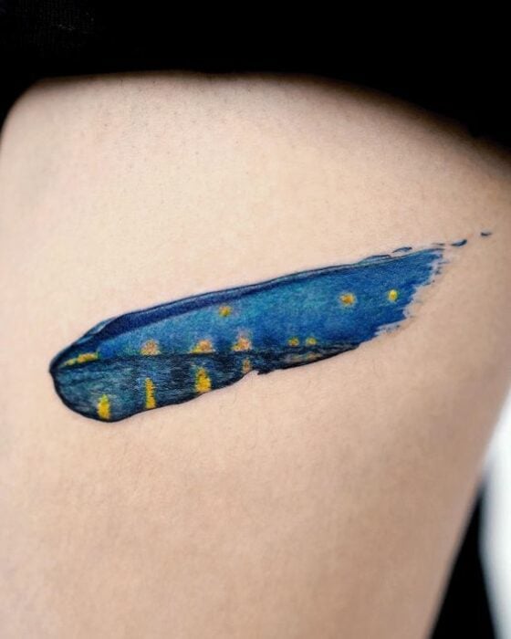 Tatuaje pequeño sobre el muslo de una pincelada de color azul con detalles amarillos