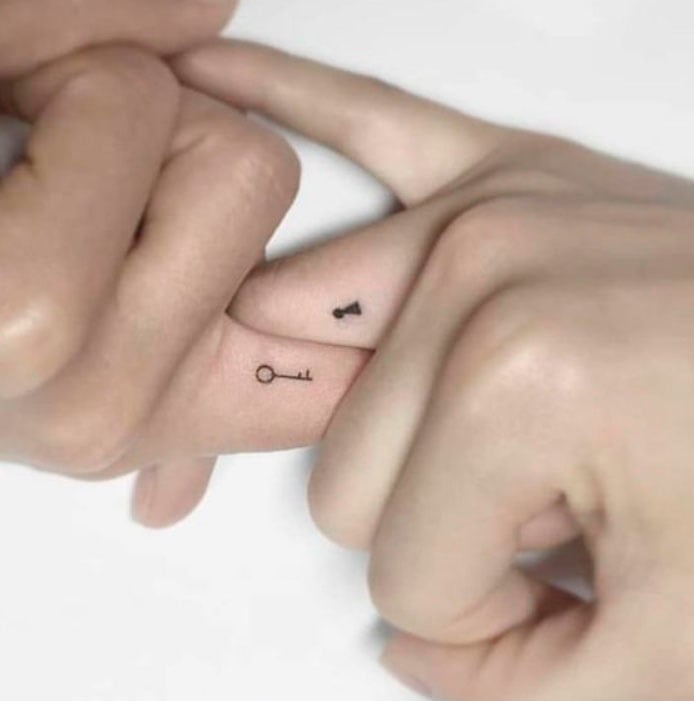Tatuaje complementario de una llave y el hoyo de una cerradura sobre los dedos