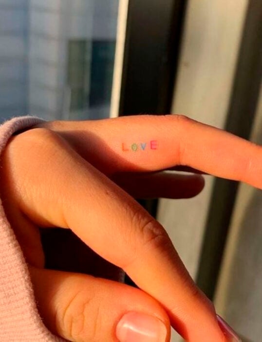 Tatuaje pequeño em la parte interna del dedo de una palabra con letras de colores