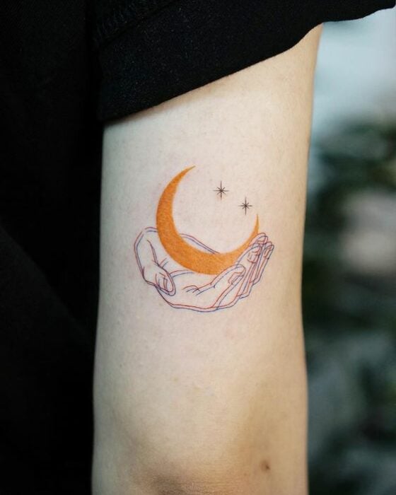 Tatuaje pequeño sobre el antebrazo de una mano sosteniendo una luna