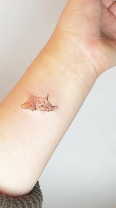 Tatuaje pequeño sobre la muñeca de un gatito durmiendo 