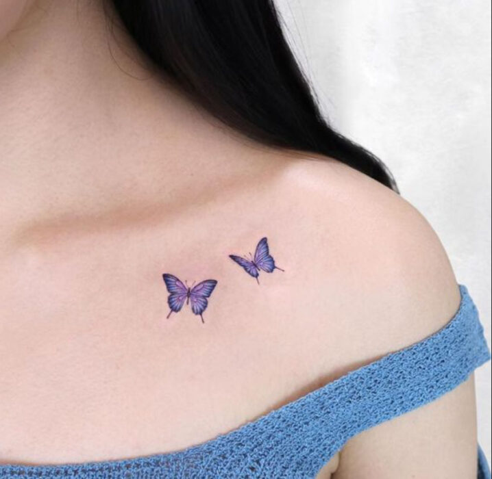 Tatuaje pequeño sobre la clavícula, de dos mariposas color morado