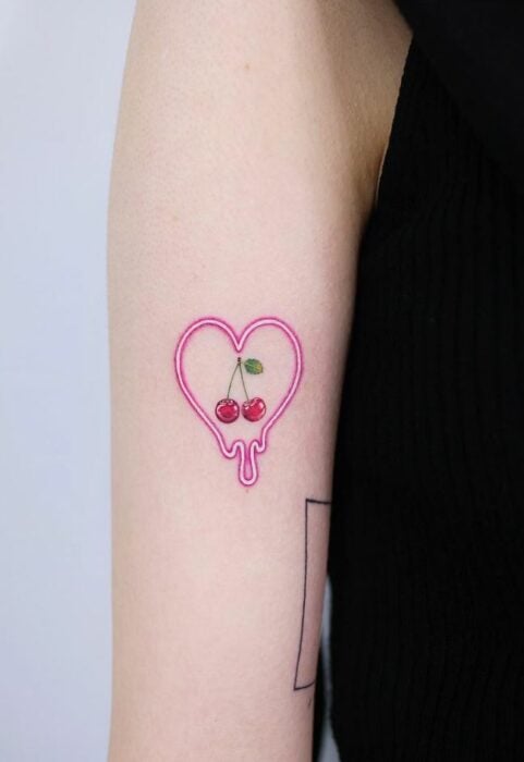 Chica con un tatuaje de color rosa en forma de corazón con cerezas