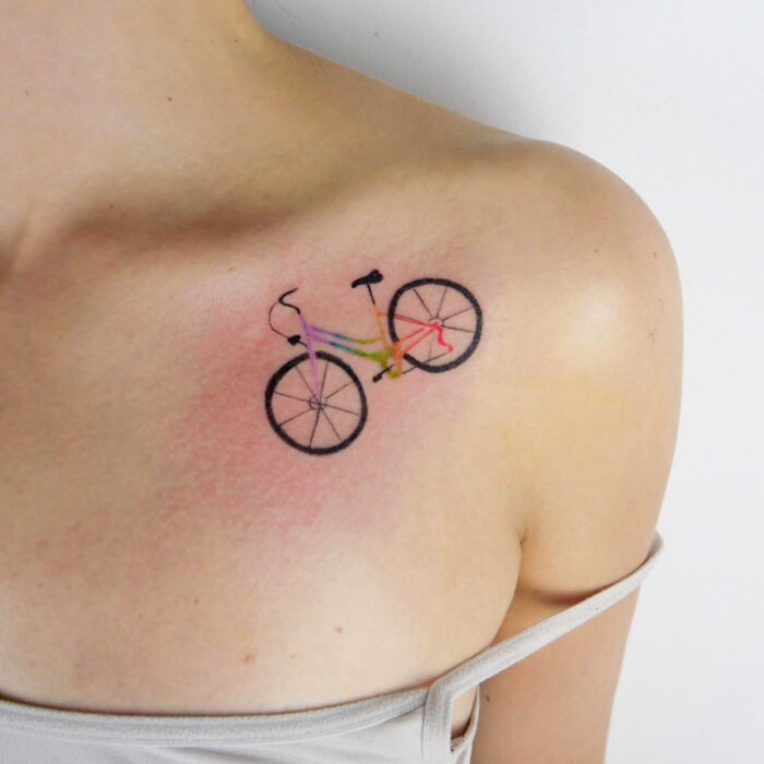 Diseños bonitos de tatuajes de bicicleta de colores arcoíris en la clavícula