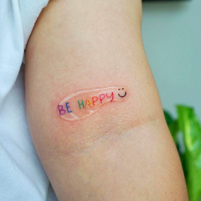 Diseños bonitos de tatuajes de palabras Be Happy de colores arcoíris en el brazo