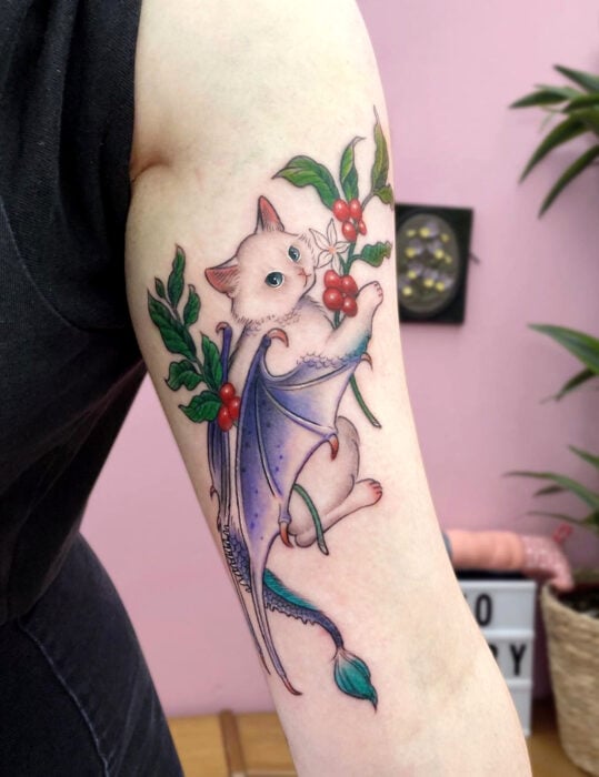 Diseños de tatuajes originales; tatuaje surrealista en el brazo de gato blanco con ojos azules y alas de dragón,