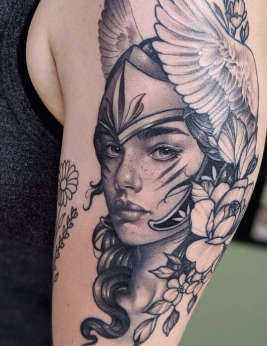 Diseños de tatuajes originales; tatuaje en blanco y negro de rostro realista de guerrera amazona en el brazo