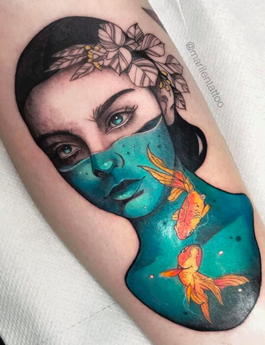 Diseños de tatuajes originales; mujer de ojos azules con pecera con peces dorados, tatuaje surrealista en la pierna