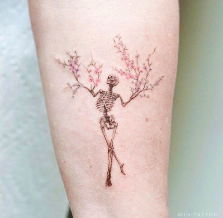 Chica con tatuaje en forma de calavera con ramas saliendo de los brazos