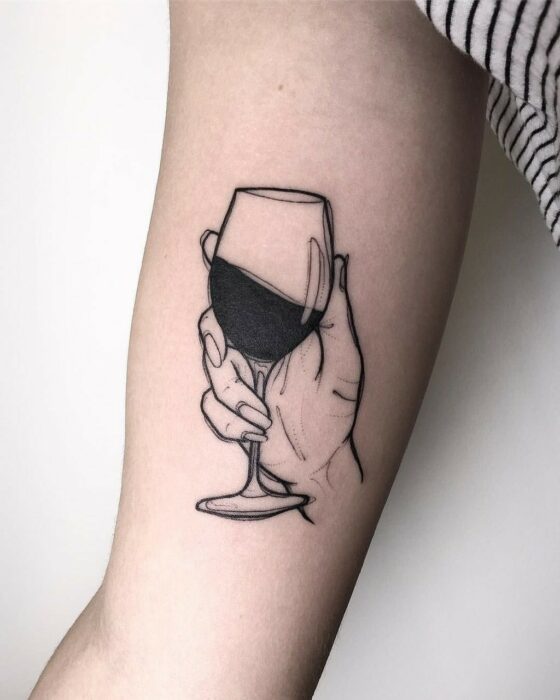 Chica con tatuaje de una mano sosteniendo uan copa de vino en el codo