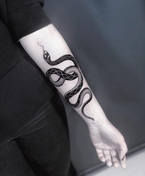 Chica con tatuaje de serpientes en color negro en el antrebrazo