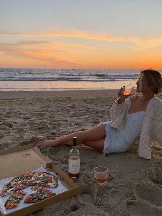 Chica tomando vino en una playa al atardecer