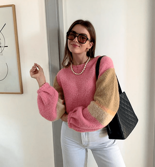 chica de cabello castaño usando lentes de sol, blusa tejida color rosa con café y beige, jeans a la cintura y bolso negro cuadrado