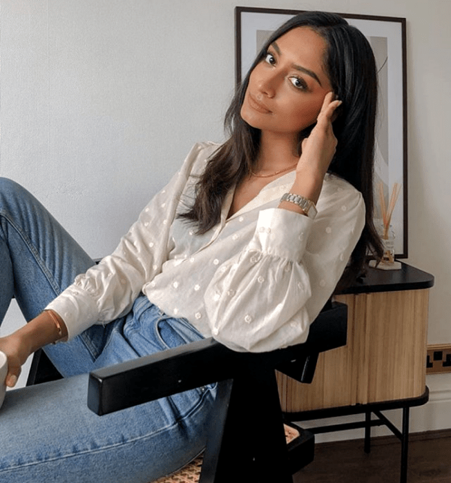 chica de cabello oscuro usando una blusa beige semitransparente con cuello en V y mangas largas, lunares blancos. jeans a la cintura