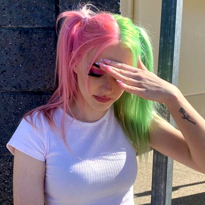chica con cabello teñido rosa y verde pastel, mitad y mitad teñido con sombra de ojos rosa y top blanco de manga larga