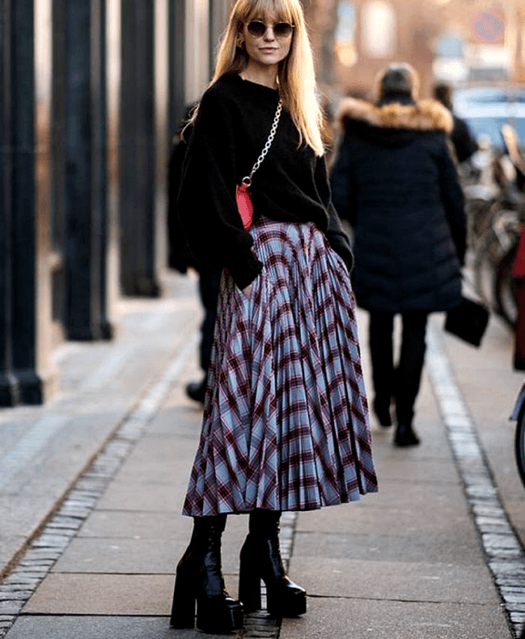 chica rubia usando lentes de sol, suéter negro, falda maxi con bolsillos azul con lineas rojas y negras, botas de plataforma negras y bolso rojo crossbody bag