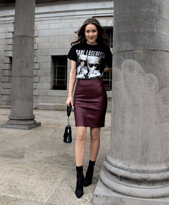 chica de cabello castaño usando una camiseta negra de karl lagerfeld, minifalda de cuero guinda, botines negros estilo sock boots y bolso de mano negro