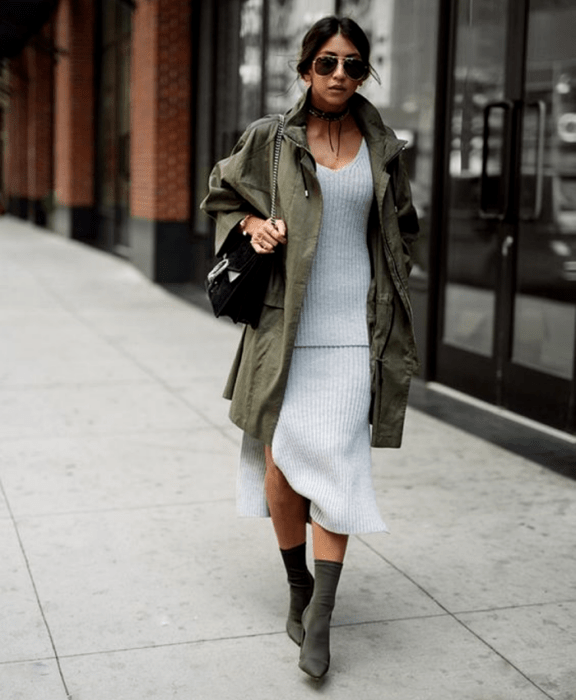 chica morena usando lentes de sol, vestido tejido gris, chaqueta larga color verde militar, bolso negro de mano y botines estilo sock boots verde militar