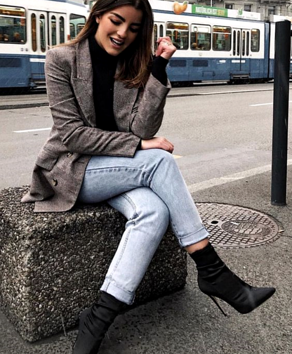 chica de cabello castaño claro usando un top negro, blazer café tejido, jeans rectos, botines negros estilo sock boots