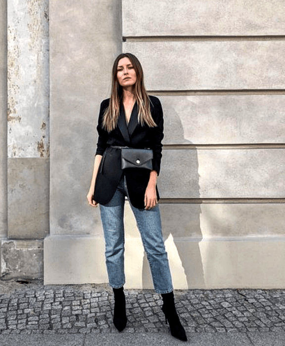 chica de cabello claro largo usando un blazer negro oversized, bolso negro estilo cangurera, jeans rectos y botines negros estilo sock boots