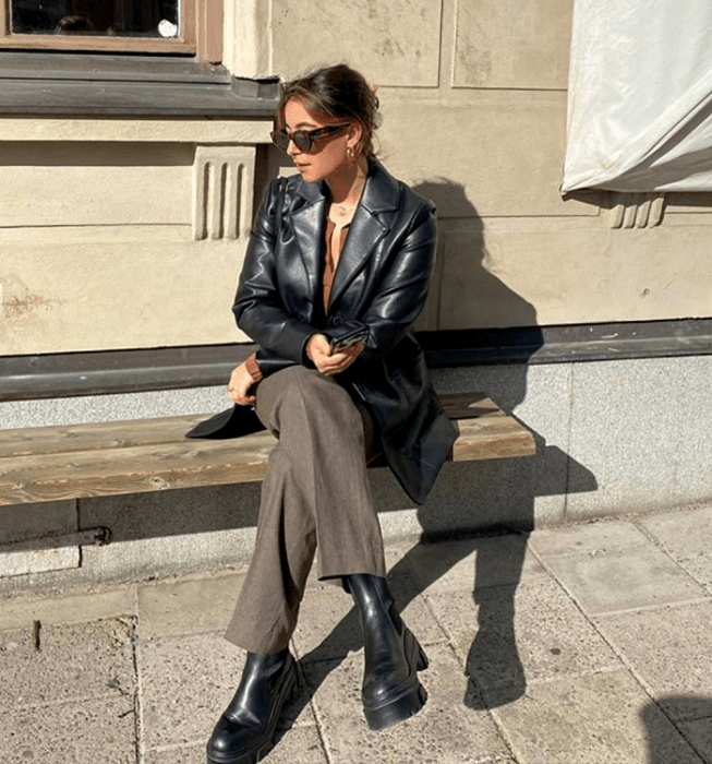 chica de cabello castaño claro usando lentes de sol, blusa café, abrigo de mezclilla, pantalones de vestir cafés, botas negras de plataforma