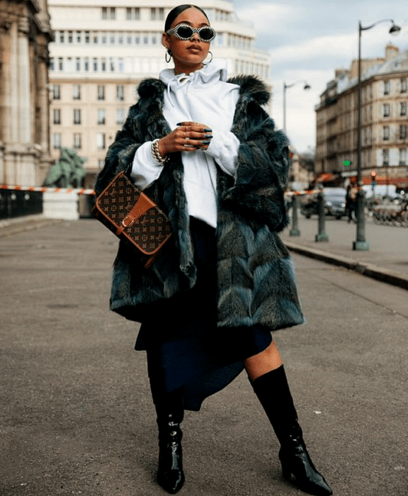 chica morena usando lentes de sol, sudadera blanca, abrigo afelpado azul con vetas negras, falda midi azul marino, botas largas de cuero negro con tacón y bolso café LV