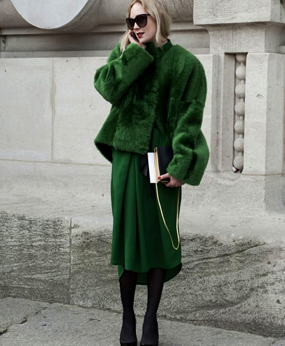 chica rubia usando lentes de sol, abrigo afelpado verde, vestido midi verde, medias negras, zapatos de tacón y bolso negro de mano