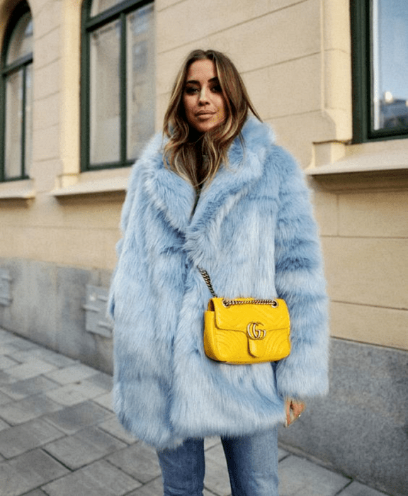 chica de cabello claro usando un abrigo afelpado azul celeste, bolso amarillo crossover y jeans