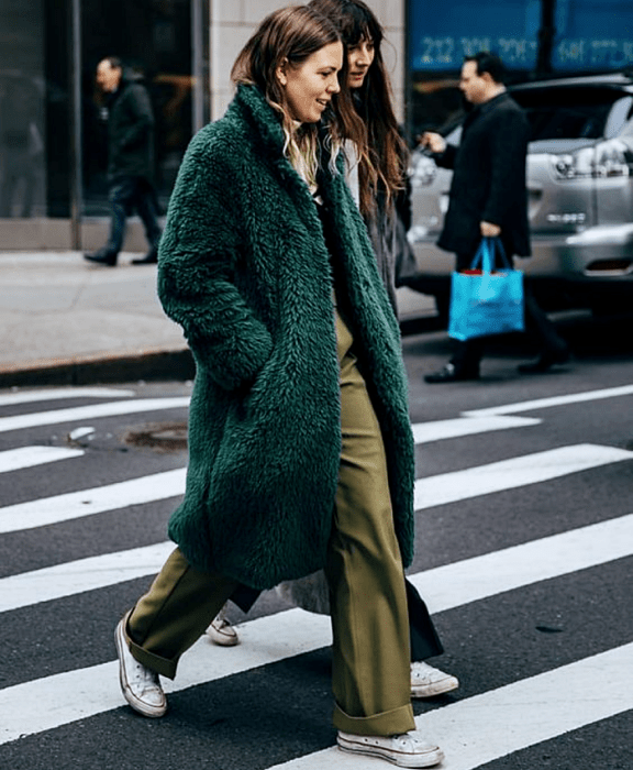 chica de cabello castaño usando un abrigo afelpado verde oscuro, pantalón de vestir verde olivo, tenis converse blancos y top beige