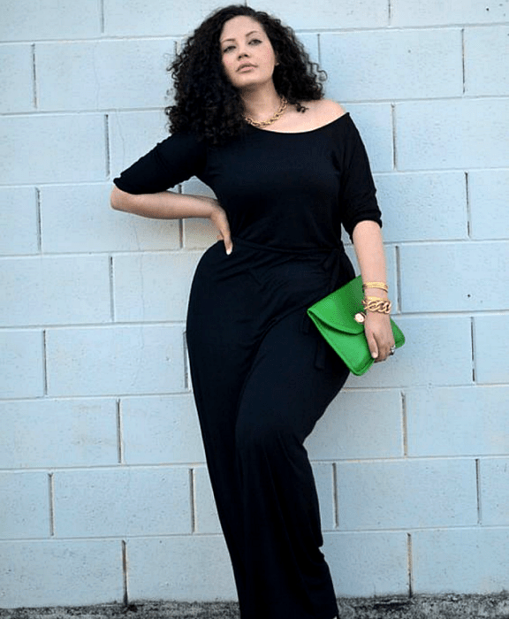 chica curvy de cabello chino usando un jumpsuit azul marino con mangas 3/4 y bolso verde de mano