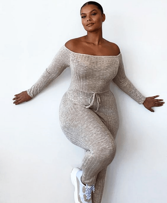 chica morena curvy usando un jumpsuit beige tejido tipo suéter, a los hombros con manga larga, ajuste a la cintura y tenis deportivos blancos con beige