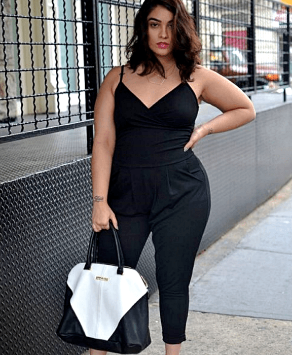 chica curvy de cabello castaño usando un jumpsuit negro de tirantes con escote en V y pantalón tipo de vestir, bolso blanco con negro de piel