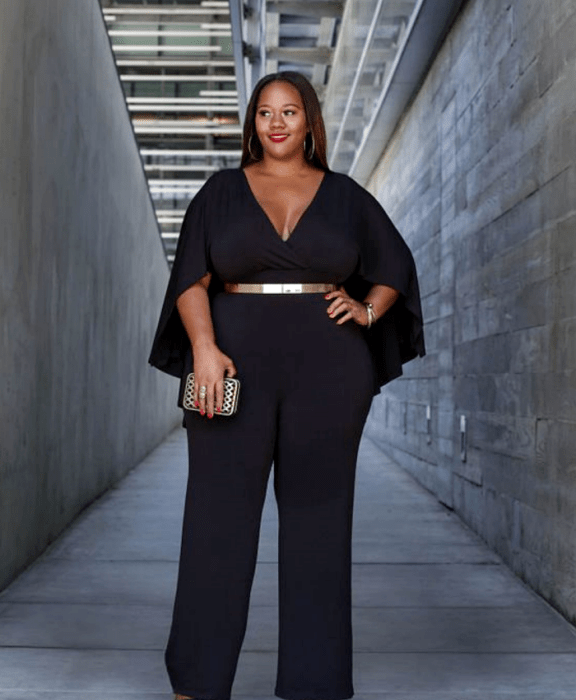 chica morena curvy usando un jumpsuit negro de mangas amplias, escote en v, cinturón dorado metálico y bolso clutch de mano metálico dorado