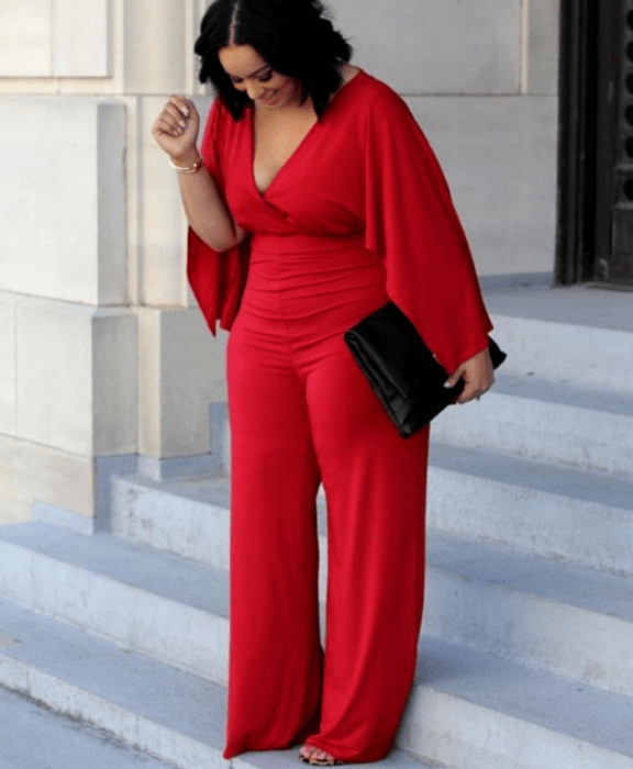 chica morena curvy usando un jumpsuit rojo con mangas holgadas largas, escote en v, pantalón largo, bolso de mano negro de piel