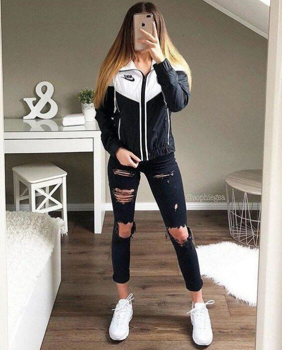 Chica usando jeans rasgados con tenis de color blanco y una chaqueta de color blanco con negro