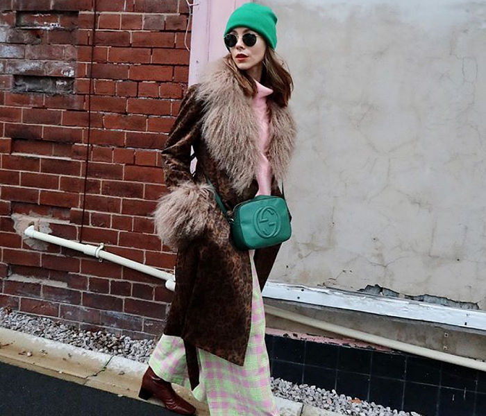 chica de cabello castaño con lentes de sol, gorro verde, suéter rosa, abrigo café de piel afelpado, pantalones culotte rosas con verde, botines cafés y bolso verde