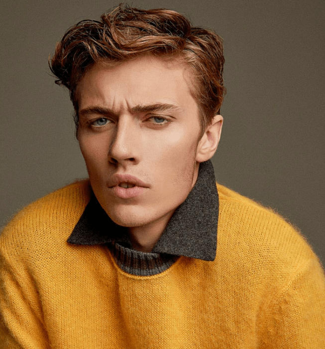 Lucky Blue Smith; chico rubio de ojos azules con una camisa de vestir gris, un suéter amarillo intenso