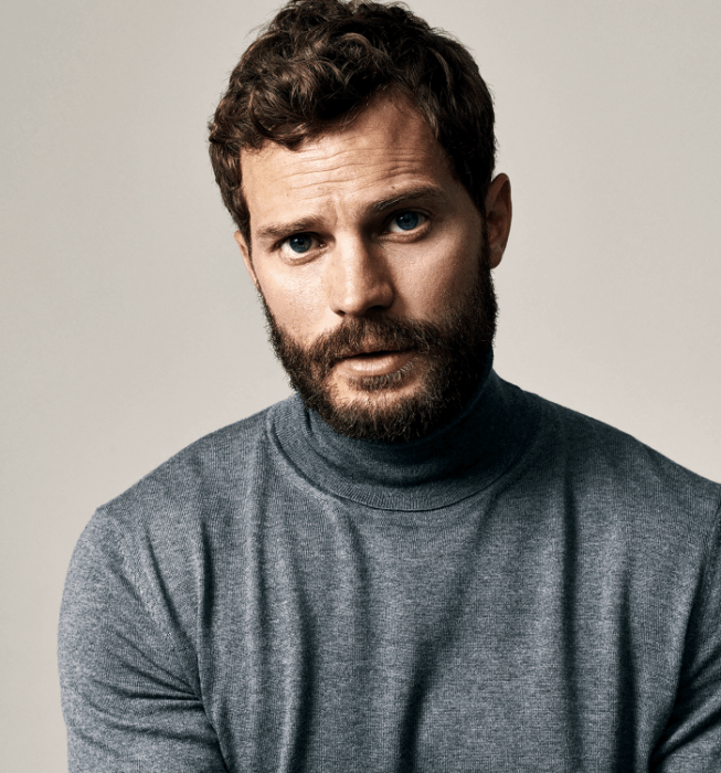 Jamie Dornan; chico de cabello castaño con barba usando un top gris de cuello alto y manga larga