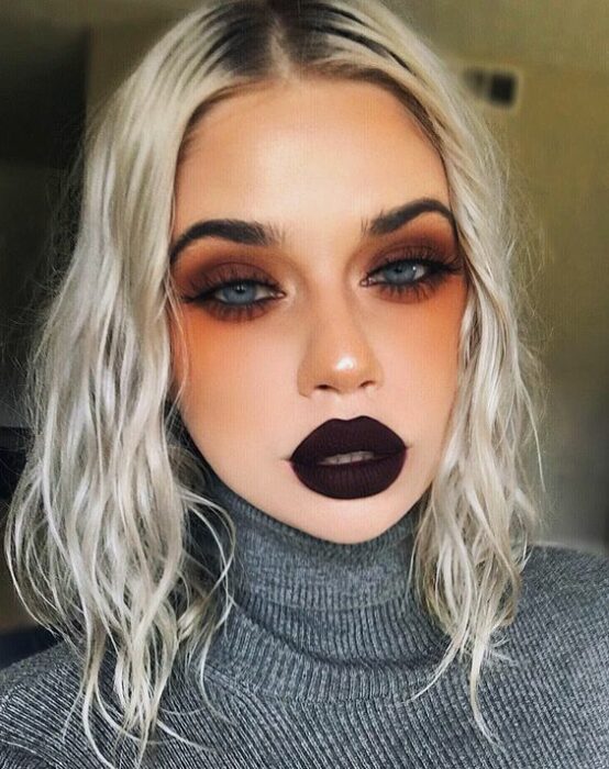 Chica rubia de cabello platinado con labial oscuro y sombras de ojos naranjas con café