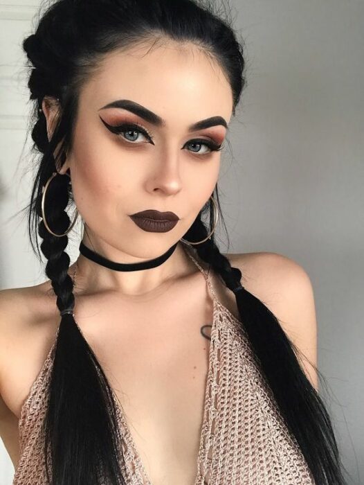 Chica blanca con peinado de trenzas y maquillaje de sombras y labial oscuro 