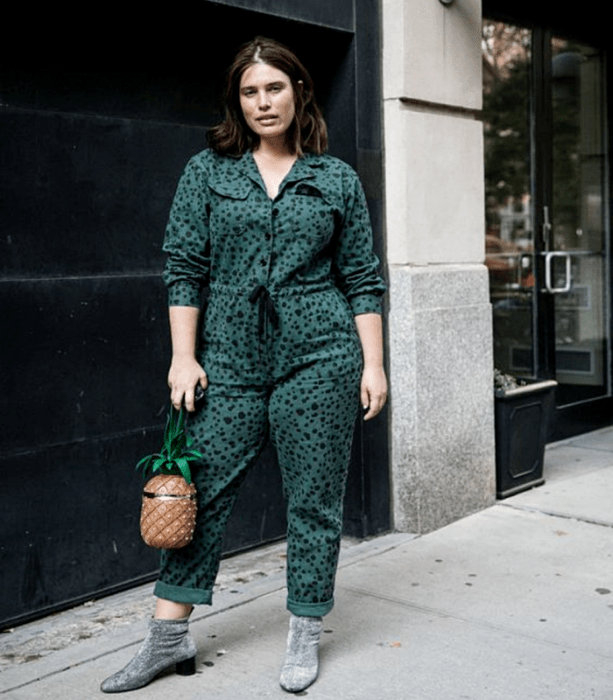 chica curvy de cabello castaño corto usando un jumper, mono color verde con lunares negros, botines de terciopelo gris con tacón negro y bolso de mano en forma de piña