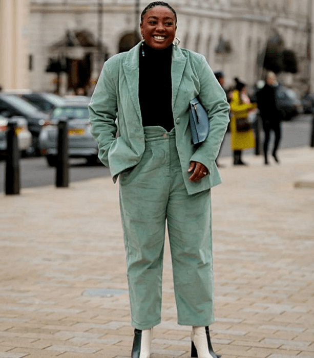 chica curvy morena usando un suéter negro de cuello alto, saco verde menta de pana, pantalones de vestir color verde menta de pana, botines de piel beige con verde y bolso de mano azul celeste