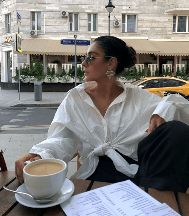 chica de cabello castaño usando lentes de sol, camisa oversized blanca, pantalones de vestir negros