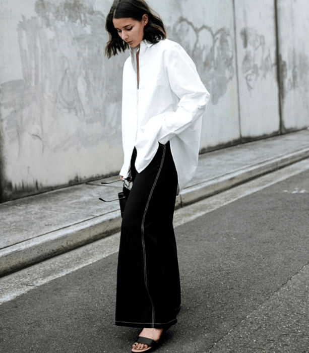 chica de cabello castaño usando una camisa oversized blanca, pantalones tipo culotte negros y sandalias negras