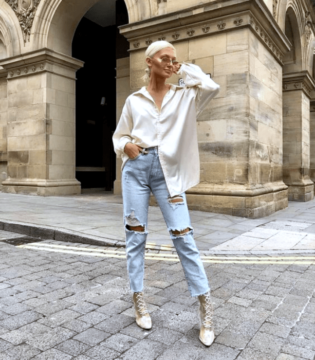 chica rubia usando lentes de sol, camisa oversized blanca, jeans rasgados, botines beige de tacón con agujetas 