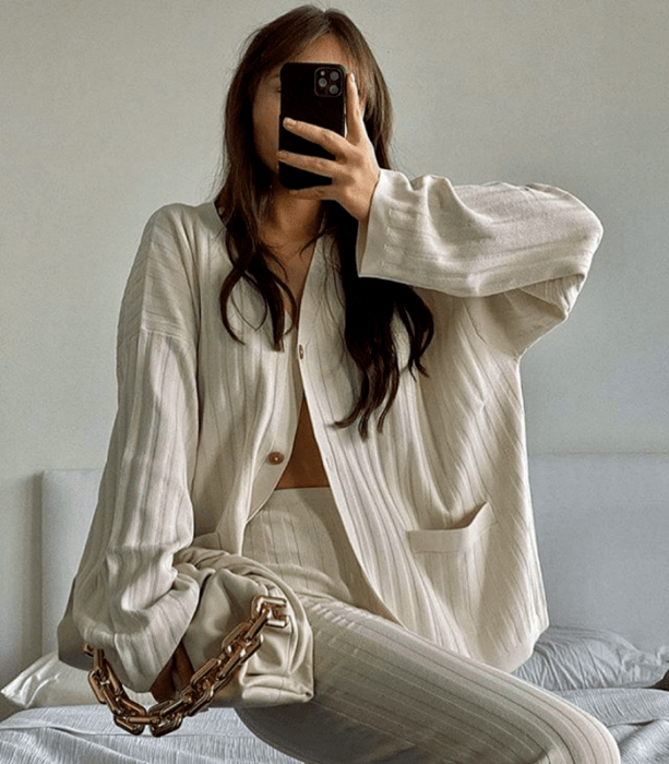 chica de cabello claro usando una camisa oversized blanca beige tejida, patalones de vestir tejidos beige y bolso de mano beige con cadena dorada