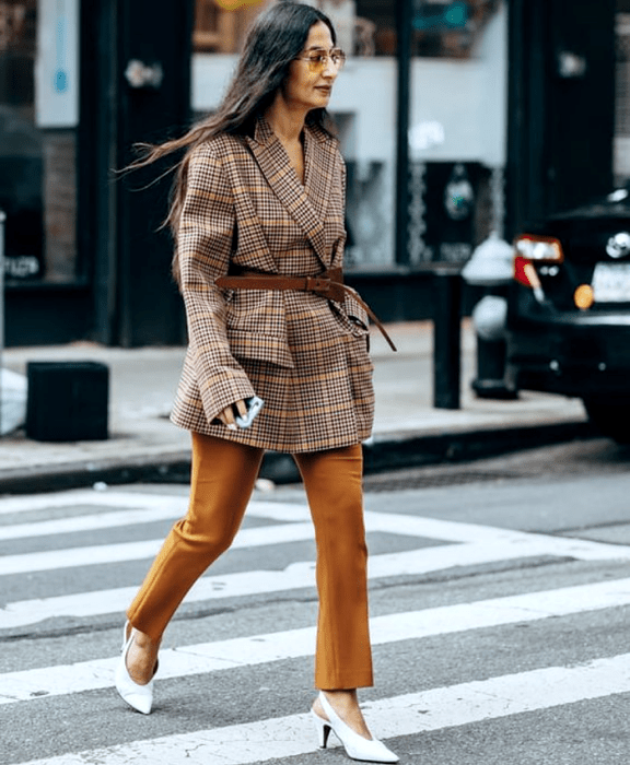 chica de cabello castaño largo usando un blazer oversized café de cuadros, cinturón café, pantalones cafés de vestir y zapatos blancos de tacón