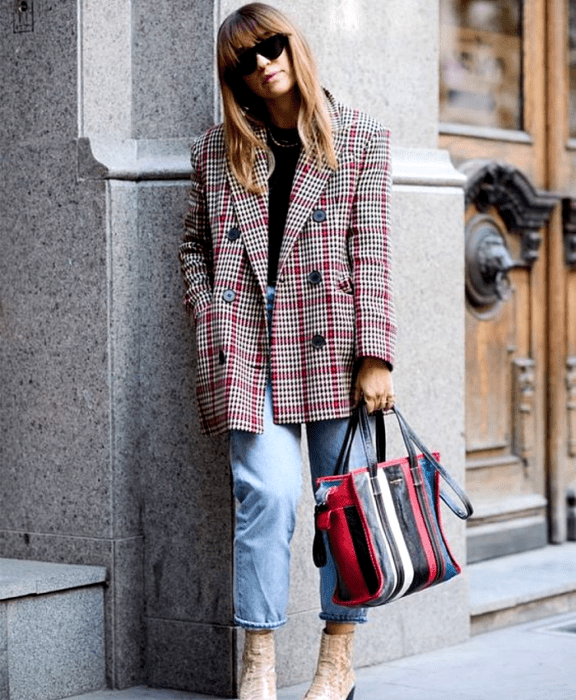 chica de cabello rubio usando lentes de sol, top negro, blazer gris de cuadros rojos, mom jeans a la cintura, botines de piel beige, bolso de mano rojo, blanco, azul y negro