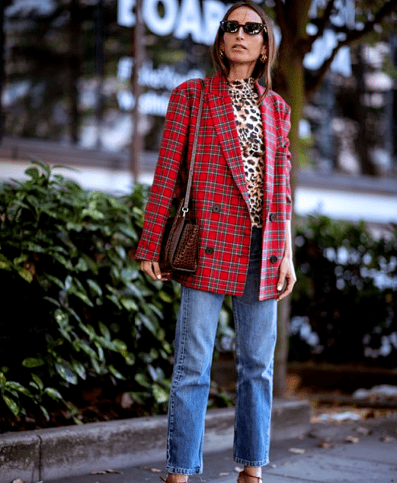 chica de cabello claro usando lentes de sol, top estampado de animal print, blazer rojo de cuadros, jeans rectos, bolso café de cuero