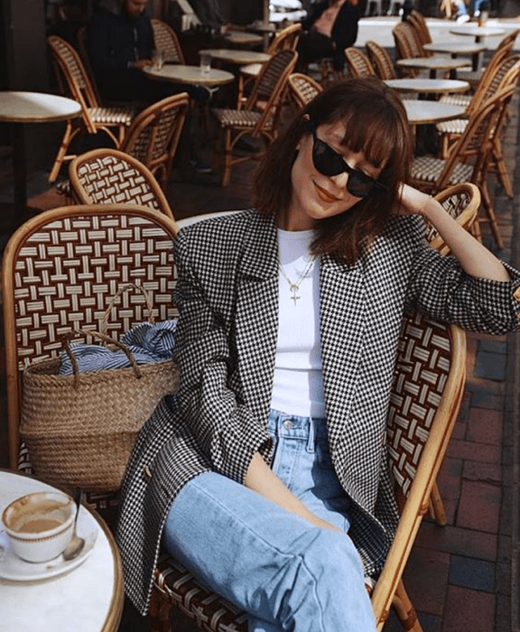 chica de cabello castaño usando lentes de sol, top blanco, blazer blanco con negro de cuadros, jeans a la cintura